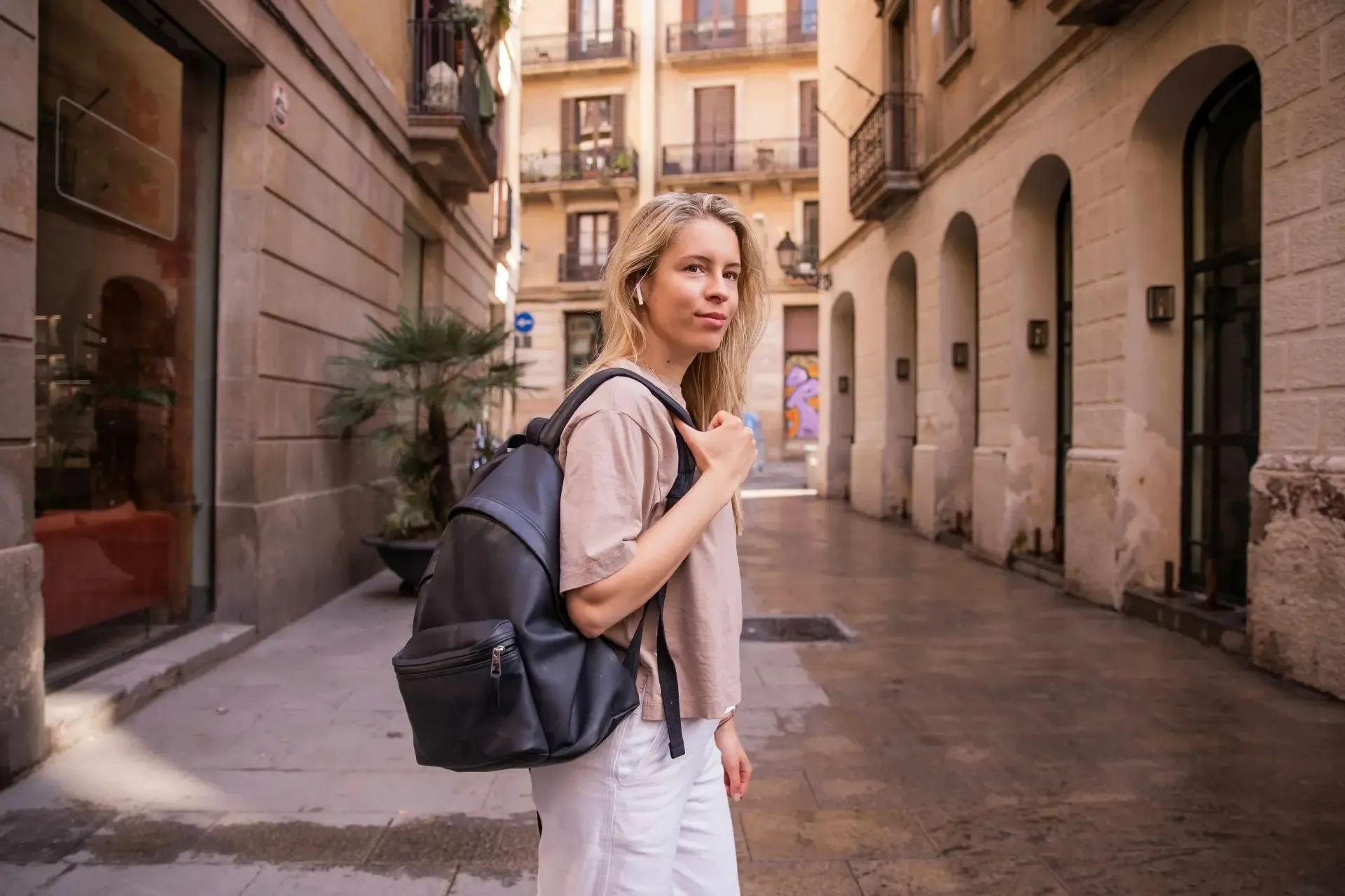 Nuori expat-matkailija reppuselässä kävelemässä aurinkoisella espanjalaisella kadulla, edustaen matkavakuutusta Espanjasta